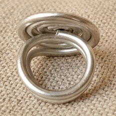 "Anello a spirale in alluminio anodizzato argento vista laterale dettaglio struttura su tessuto lino naturale"