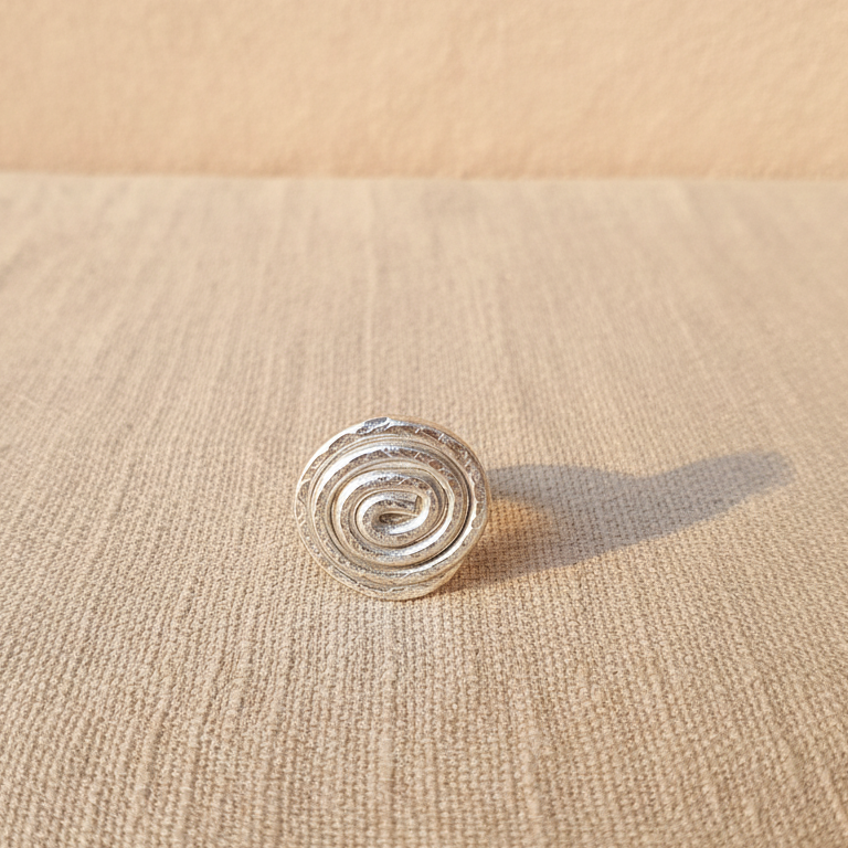 "Anello a spirale in alluminio anodizzato argento vista frontale dettaglio intreccio su tessuto lino naturale"